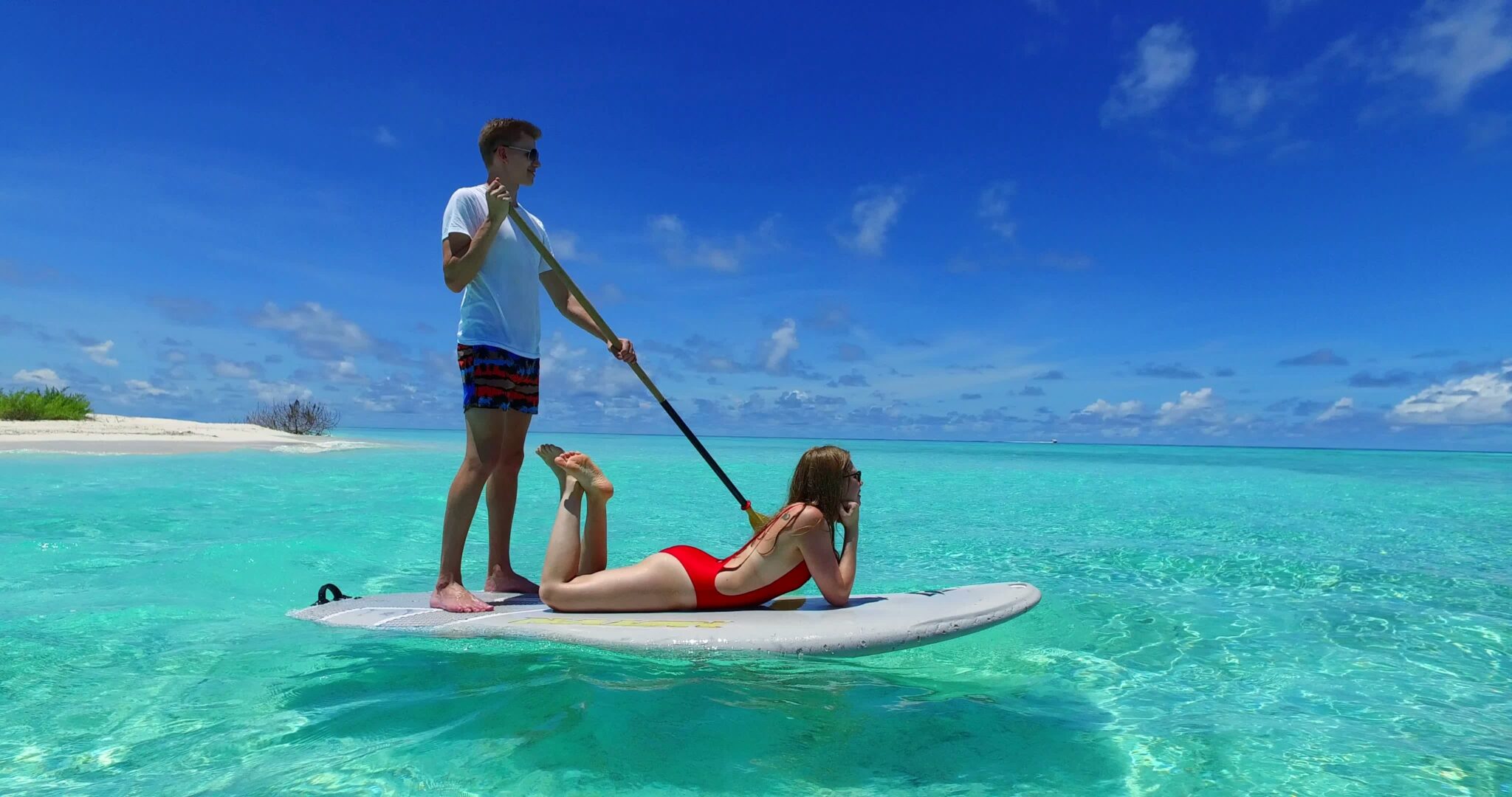 Male and female couple on white stand-up paddle boarding on turquoise ocean in Turks and Caicos